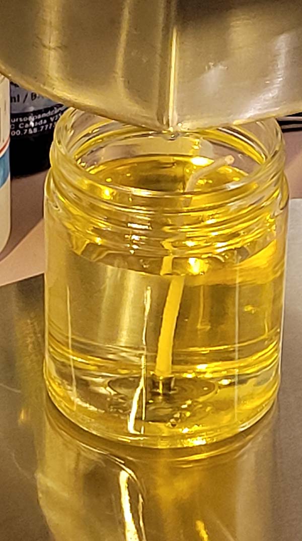 picture of pouring the last drop of melted soy wax into candle jar with wick